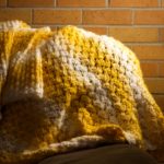 yellow and white blanket draped on a couch in front of a brick wall